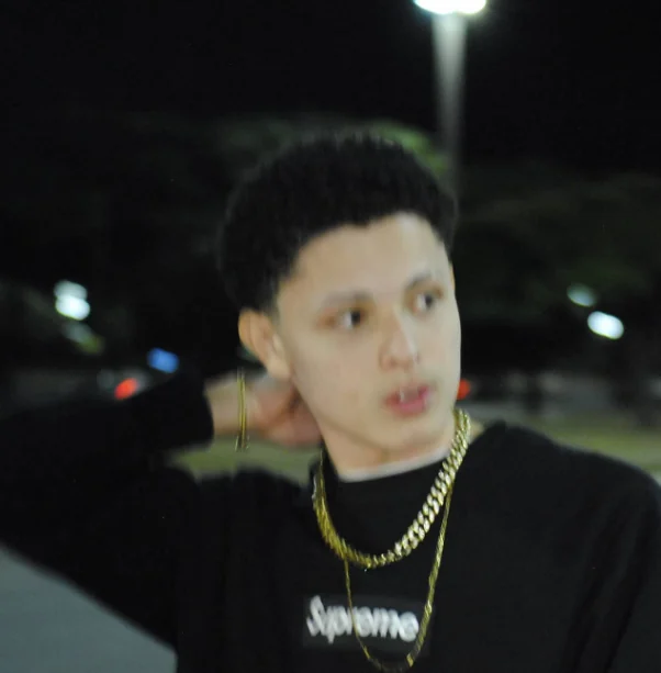 A motion-blurred night portrait of Thalles Leal dressed in black with golden chains.