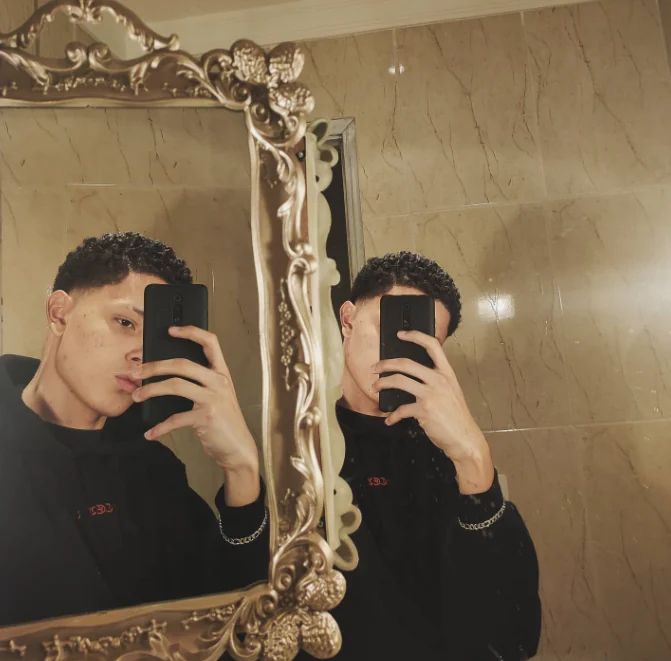 Thalles Leal reflected in an ornate golden mirror in a marble setting.